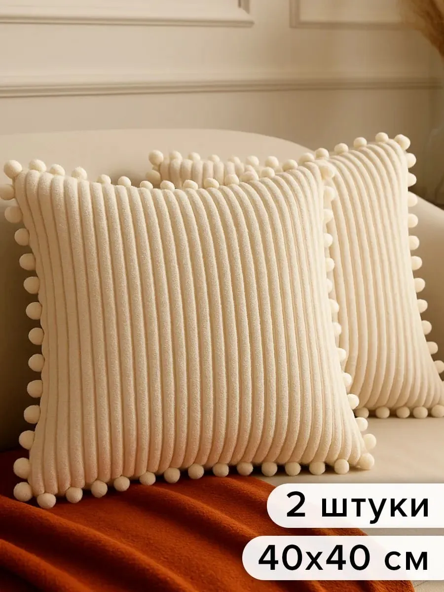 Две декоративные подушки 40×40 см в кремово-бежевом рубчике с помпонами по краю, уютный текстильный декор на оранжевом пледе
